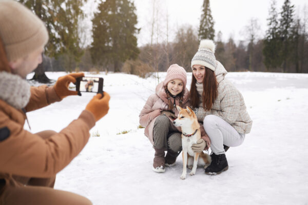 Family enjoying a winter park outing, taking photos together with their dog in the snow.