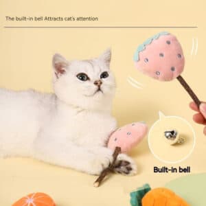 Fluffy white cat mesmerized by colorful plush fruit toys against a cheerful yellow background.