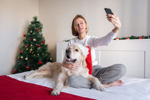 Joyful holiday selfie with woman and golden retriever by a decorated Christmas tree.