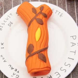 Vibrant orange log-shaped dessert with chocolate leaves on a whimsical plate, perfect for celebrations.