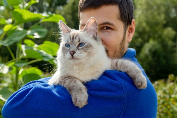 A man lovingly holds a cat outdoors, showcasing their strong bond in natures beauty.