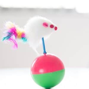 Playful mouse toy with colorful feathers atop a vibrant split ball for imaginative play.