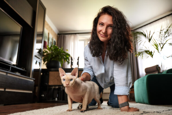 Young woman hugging hairless cat on a cozy rug in a bright living room.