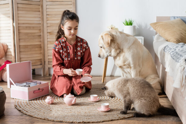 Young girl enjoying a whimsical tea party with her dog and cat on the floor.