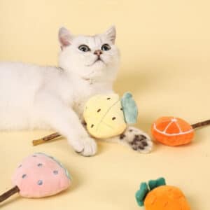 Charming white cat playing with colorful fruit toys against a soft yellow background.